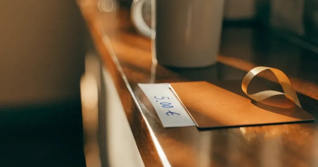 Un biglietto regalo con un nastro dorato accanto a una schedina su un bancone di legno